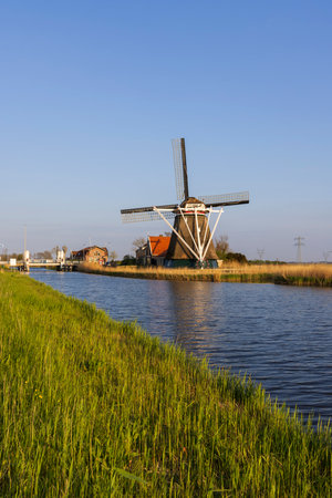 Scenic view of a historic windmill by a canal in Heerhugowaard, North Holland, showcasing Dutch countryside charmの写真素材