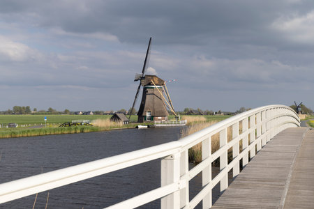 Picturesque view of a traditional Dutch windmill in Groot Ammers, South Holland, with a white wooden bridge over the canalの写真素材
