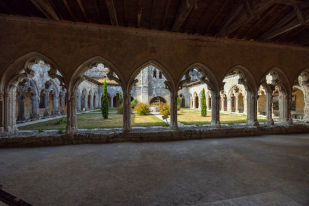 Stone arches framing a courtyard garden with cypress trees and a central fountain in the cloister of the Collegiate Church of Saint Pierre in La Romieu, Franceの写真素材