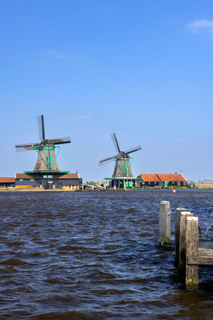 Traditional Dutch windmills stand tall against a clear blue sky in Zaandijk, Netherlandsの写真素材