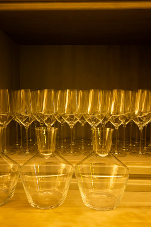 Wine glasses and decanters standing on a wooden shelf in warm light, ready for a celebration or a dinner partyの写真素材