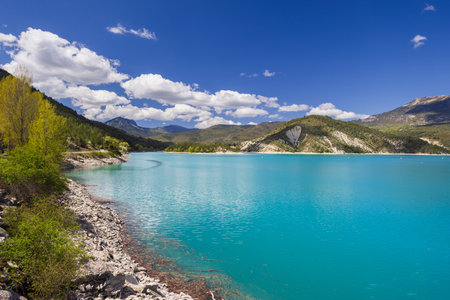 Turquoise water of Castillon Lake reflecting blue sky with white clouds in Castellane, Alpes de Haute Provence, Provence Alpes Cote d'Azur, Franceの写真素材