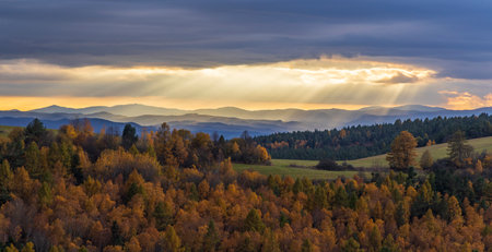 Sun rays shining through clouds over colorful autumn forest landscape with Low Tatras