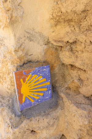 Colorful tile with yellow scallop shell, symbol of the Camino de Santiago, embedded in a stone wall in Castrojeriz, Burgos, Spainの写真素材