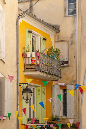 Festive decorations hanging between colorful buildings with plants on a balcony in Nyons, Franceの写真素材