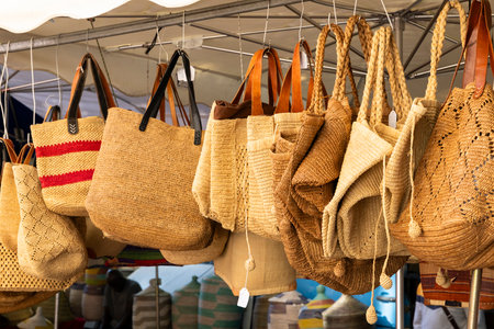 Raffia bags hanging from the roof of a market stall in Nyons, France, during a sunny dayの写真素材