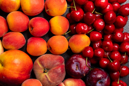 Vibrant display of fresh summer fruits including peaches, apricots, cherries, and plums, showcasing their ripe colors and texturesの写真素材