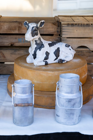 Cow figurine resting on cheese wheels with milk cans in a market stall in Nyons, France, representing local products and agricultureの写真素材