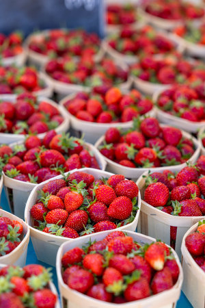 Ripe red strawberries overflowing from small wooden baskets at a farmers market in Nyons, France, creating a vibrant display of fresh produceの写真素材