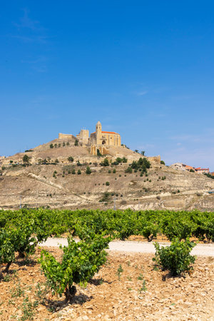 The medieval castle and church of San Vicente de la Sonsierra rising above a vineyard in La Rioja, Spain, under a clear blue skyの写真素材