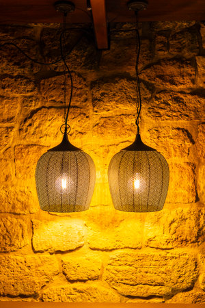 Two illuminated metal lamps hanging from a wooden beam against a yellow stone wall, creating a warm and inviting atmosphere in Gnas, Styriaの写真素材