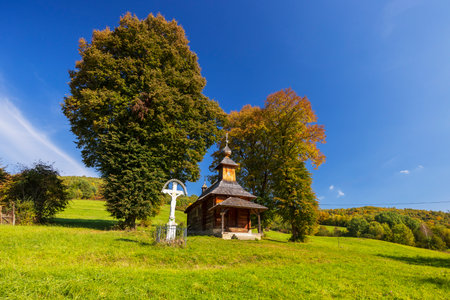 Wooden church of St. Michael the Archangel with a white cross standing on a green hill in Jalova, Slovakia, during a sunny autumn dayの写真素材