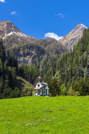 Scenic view of a small chapel nestled in a green meadow surrounded by the majestic Austrian Alps in Pragraten am Grosvenedigerの写真素材