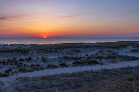 Scenic view of a vibrant sunrise painting the sky over the North Sea, casting a warm glow on the dunes of Petten beach in North Hollandの写真素材