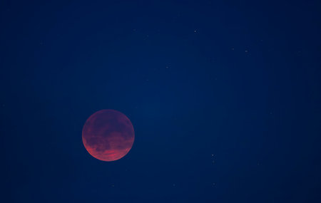 Red total lunar eclipse glowing in the dark night sky with visible stars