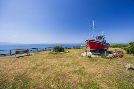 Scenic view of a red and blue fishing boat displayed on a grassy hill overlooking the Cantabrian Sea...