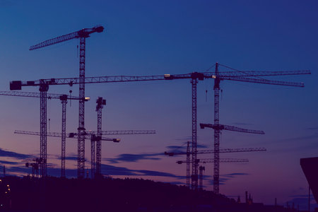 Multiple cranes silhouetted against a twilight sky in Prague, Czechia, symbolizing urban development...