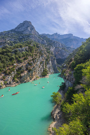 Kayakers and canoers paddling on the turquoise water of the Verdon Gorge river in France, surrounded by steep cliffs and lush vegetationの写真素材