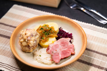 Hearty bavarian specialties with dumplings, roasted pork, sauerkraut and caramelized onions as a closeup on a plateの写真素材