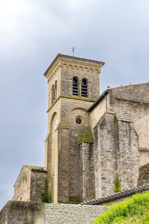 Saint Hilaire Abbey church rising majestically over a stone wall under a cloudy sky in Saint Hilaire, Aude, Franceの写真素材