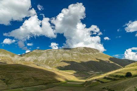 Valleys and hills of the Sibillini mountains under a blue sky with white cloudsの写真素材
