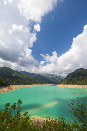 Sauris lake with turquoise water fills the mountainous landscape under a cloudy skyの写真素材