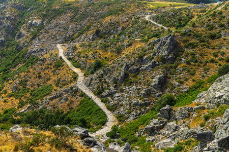 Stone road winding through a rugged mountain landscape under a clear sky in Castilla and Leon, Spainの写真素材