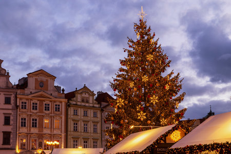 Prague Old Town Square hosting a festive Christmas market with a brightly lit Christmas tree at duskの写真素材
