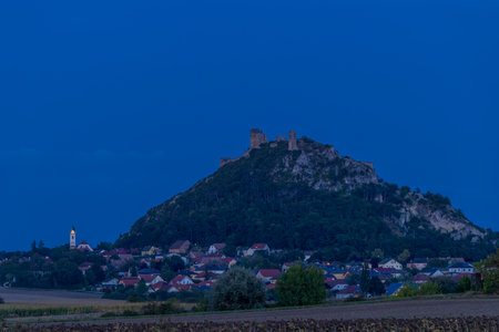 Staatz castle ruins standing atop a hill, with the village and church below during blue hourの写真素材