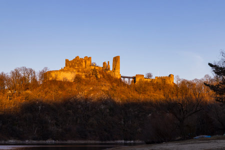 Ancient Bitov castle ruins illuminated by warm sunlight at sunset overlooking the riverの写真素材