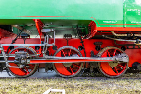 Detail of the bright red driving wheels and rods of a vintage green steam locomotive