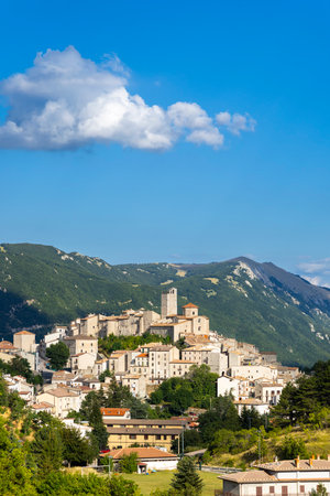 Historic Italian village and bell tower overlooking valley and green mountains under blue sky