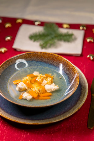 Clear broth soup with carrot slices and small dumplings serving as a festive appetizerの写真素材