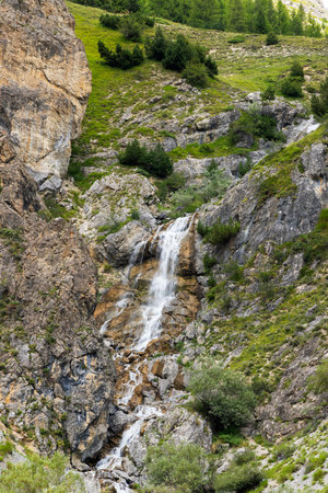 Waterfall flowing vigorously over rocks and green vegetation in the mountains of Argentera, Piedmont, Italyの写真素材