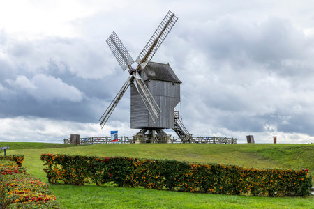 Historic post windmill standing on a grassy mound under an overcast skyの写真素材