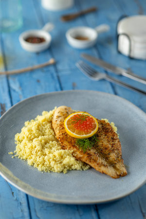Grilled fish fillet serving with couscous, lemon slice, and red caviar on a plate