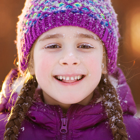 portrait of happy child close-up. winter fun outdoors. girl's face in the snowflakes. snow on violet hatの写真素材