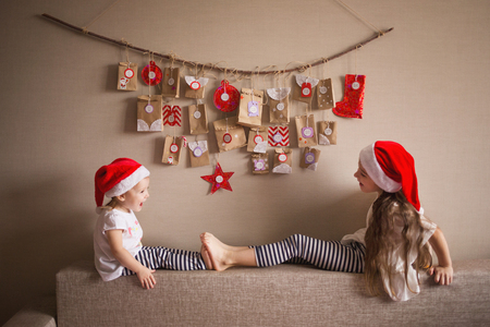 the advent calendar hanging on the wall. small gifts surprises for children. two sisters dressed as gnomes play.の写真素材