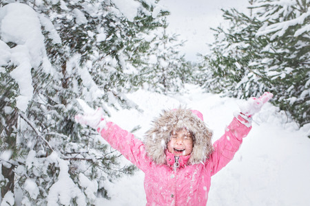 happy child in winter park. baby girl in a pink jacket throws snow outdoor.の写真素材