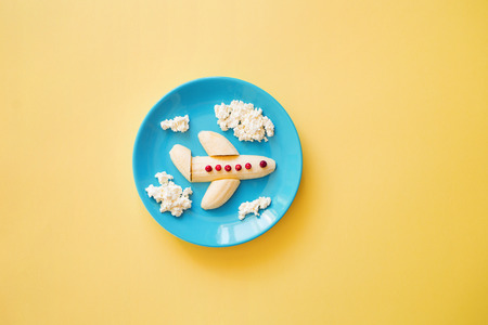 Fun food idea for kids. children's Breakfast: plane made of banana and clouds made of curd on a blue...