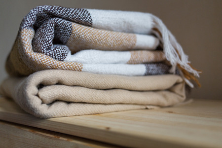 home textile. stack of beige wool blankets on a wooden shelf. autumn - winter concept of home warmth and comfort.の写真素材