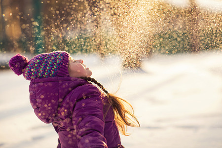 Baby girl throws the snow in frosty winter park. Flying Snowflakes. Sunny day. Child to have fun outdoors.の写真素材