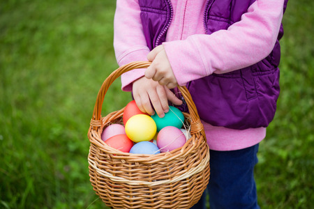 Little girl hunts Easter egg. Kids searching eggs in the garden. Child putting colorful eggs in a...