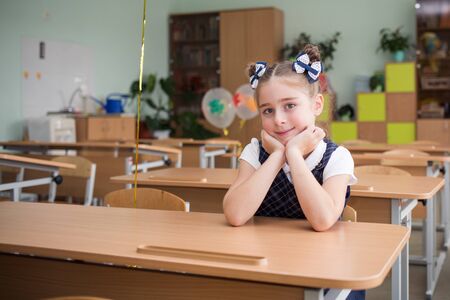 First-grader girl with bows on the first day of school at the Desk