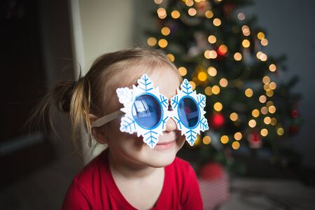 child in funny glasses in the form of snowflakes on the background of lights.