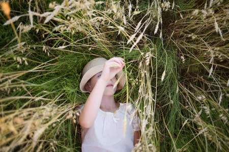 child lies on field of grain and looks at ears of wheat oats. summer rest in harmony with nature. agricultural industry.の写真素材