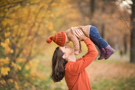 mother with child in her arms against background of autumn. family mom and baby walk in Park. kids knitted clothing hat and jacket.の写真素材