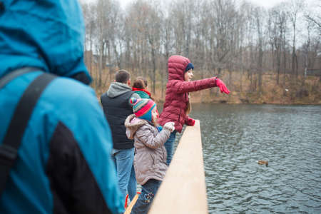family walks in the Park in autumn. dad with children to feed ducks on lake. people in October...