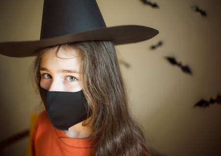 Halloween and coronovirus. portrait of child in reusable black protective mask and witch hat on background of bats.の写真素材