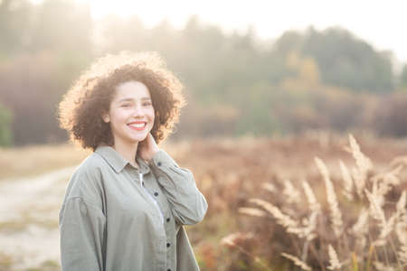 portrait of young pretty mixed race teen girl outdoor in sunlight. happy woman with finely curly hair smiles.の写真素材